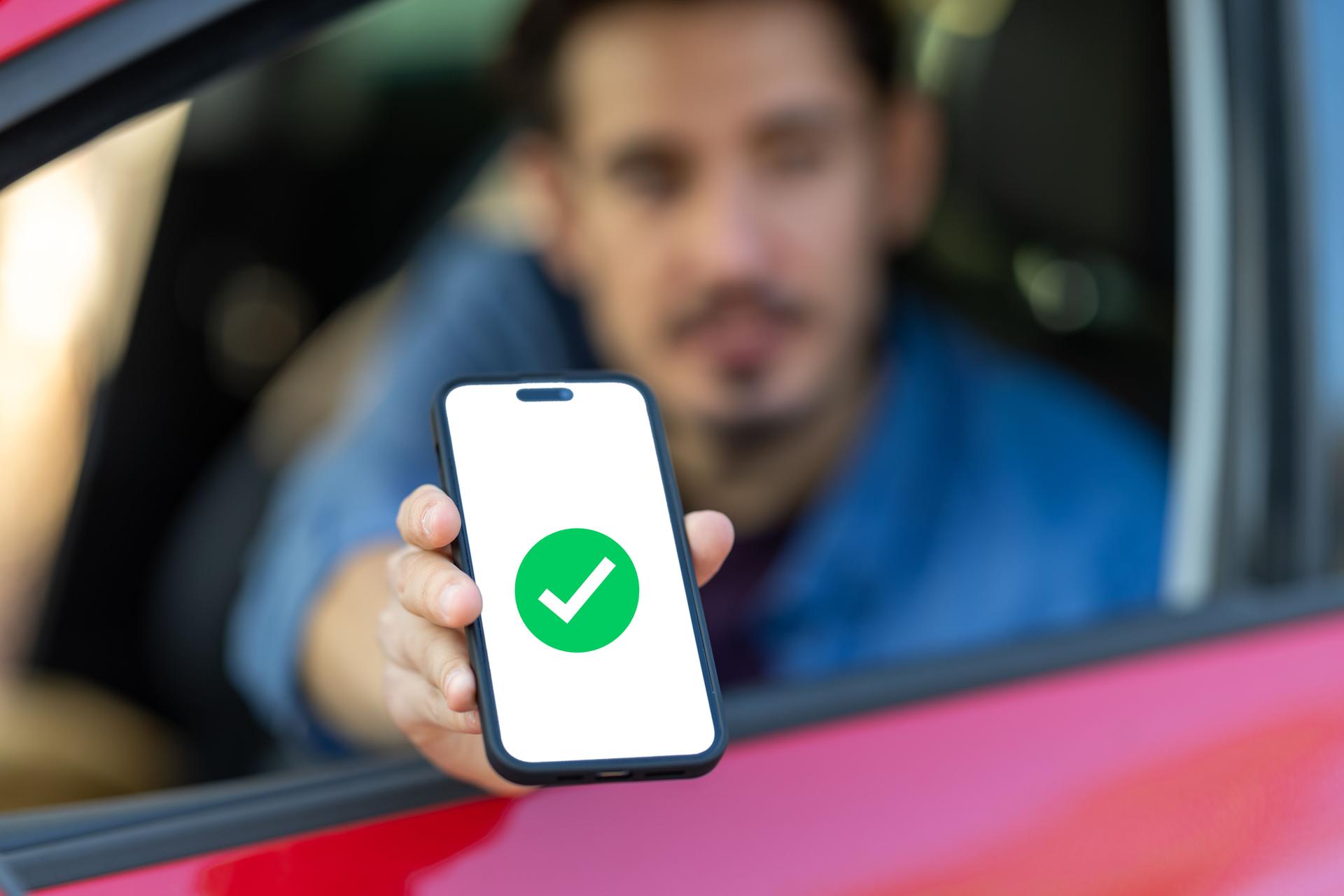 A young man traveling by car makes contactless payments with his smartphone without getting out of the vehicle.