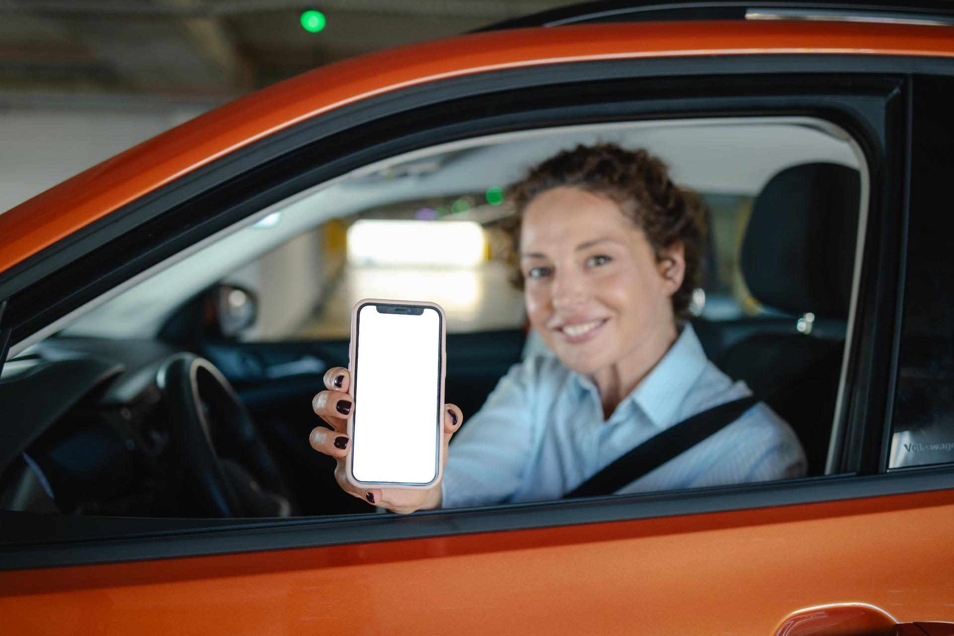 Beautiful woman showing smart phone with white screen while sitting in her car