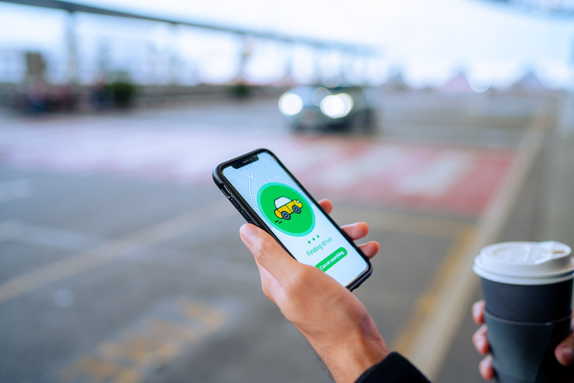 Chic young Asian man using mobile app device on smartphone to order a taxi pick up service by the urban road in downtown city street. Speedy and trustworthy service. Carsharing and business on the go themes